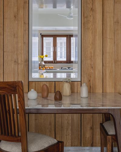 Fluted wood-panelled dining nook with stone-top table, ceramic vases, and mirror reflecting kitchen window
