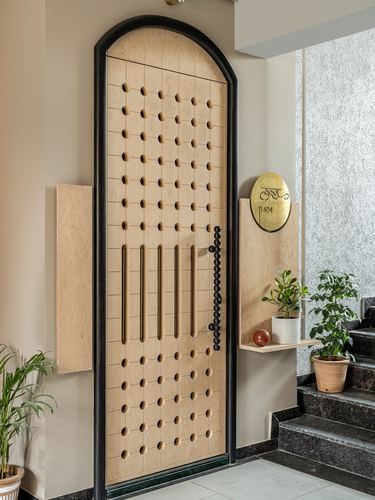 Arched black-framed wooden door with perforated pattern and brass beads at a Surat apartment entrance