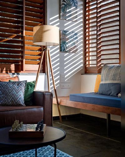 Living room corner with tripod lamp, leather sofa, and sunlight through wood louvered shutters