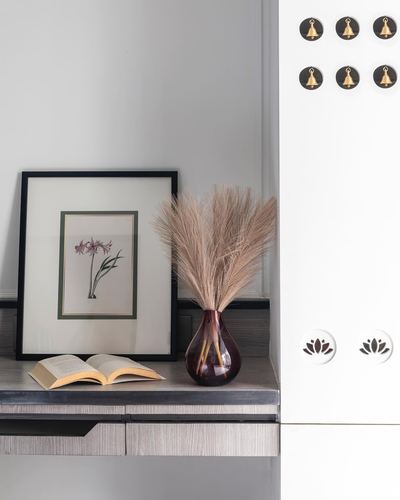 Wooden console with framed floral print, open book, and pampas grass vase beside white cabinet with bell-shaped knobs