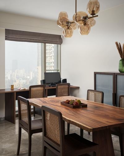 Dining table with cane chairs beneath amber glass chandelier, city skyline through window