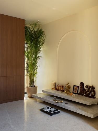 Arched niche with floating stone shelf holding brass idols beside a tall potted palm