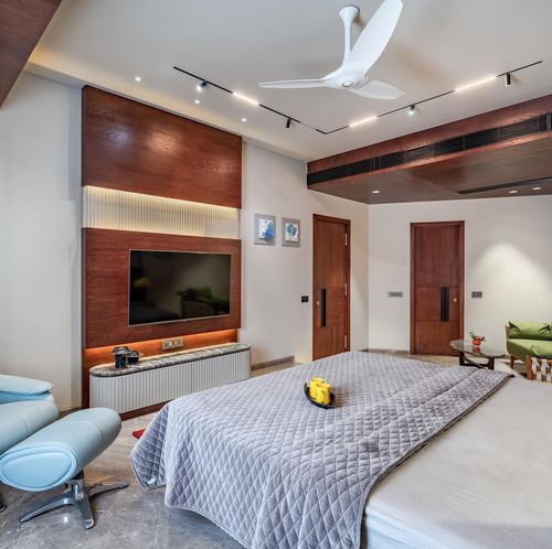 Bedroom with wood-paneled TV wall, gray quilted bedspread, and blue leather lounge chair