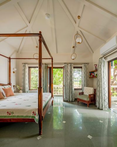 Bedroom with four-poster wood bed under vaulted truss ceiling, green stone floor, garden views