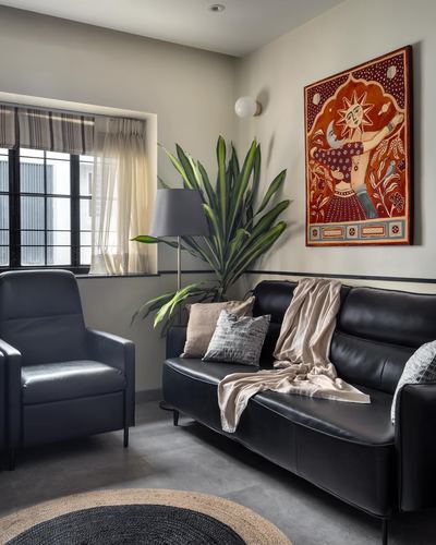 Living room corner with black leather sofa, armchair, plant, and colorful sun motif artwork on wall