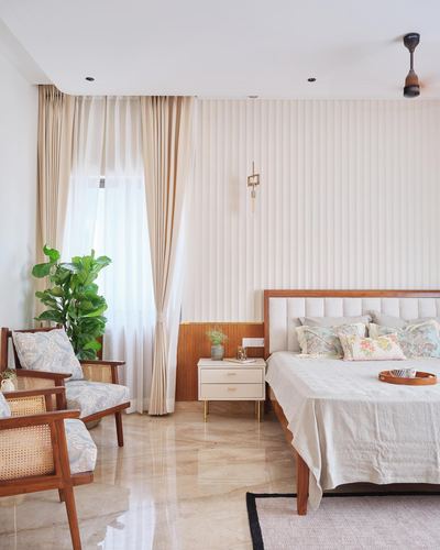 Bedroom with fluted cream wall, teak bed, cane armchairs and marble floor lit by daylight