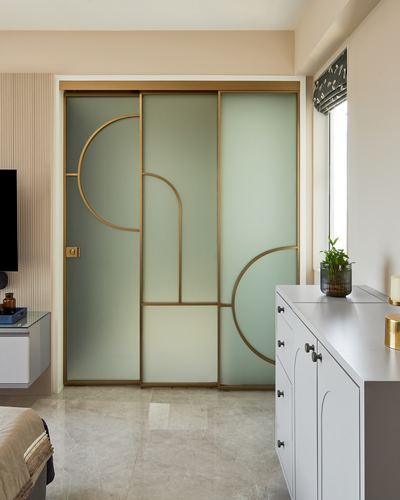 Bedroom with brass-framed frosted glass sliding wardrobe featuring arched motifs, marble floor, white scalloped cabinet