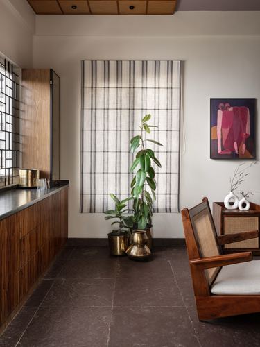 Corridor with wooden cabinetry, cane armchair, brass planters and framed artwork against stone flooring
