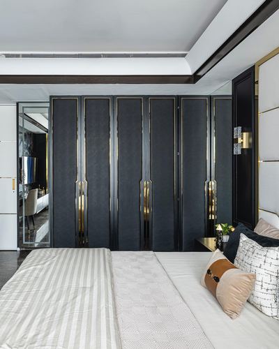 Bedroom with tall black and brass fluted wardrobe panels behind a bed with layered cushions