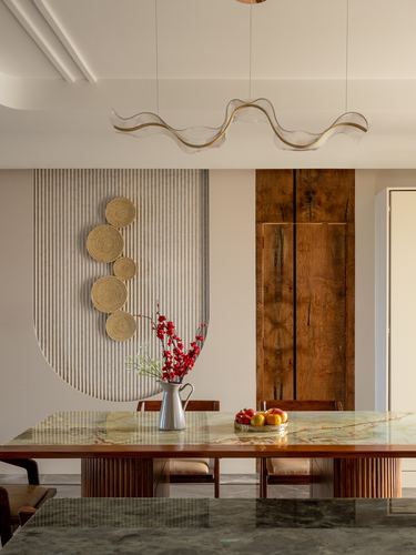 Dining table with green marble top under a wavy pendant light, woven discs and burl wood panel behind