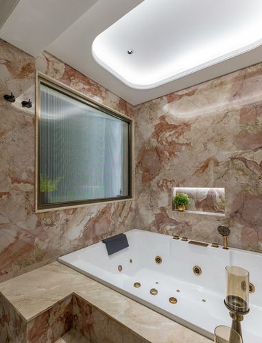 Marble-clad bathroom with jacuzzi tub, gold fixtures, and glowing ceiling cove