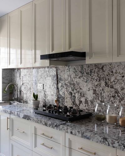 Cream cabinetry kitchen with veined marble countertop, backsplash, and black gas hob