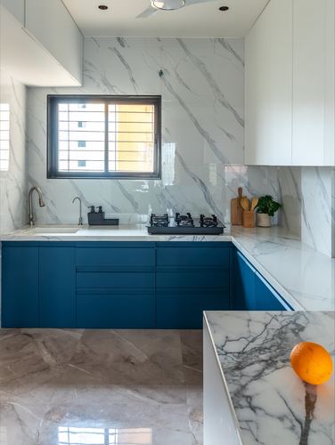 U-shaped kitchen with blue cabinets, white marble walls and countertop, window above sink