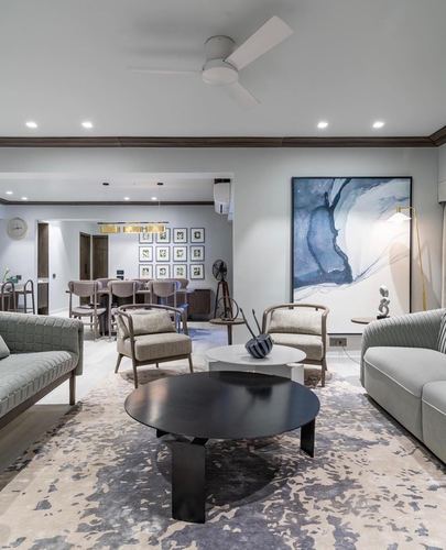 Grey and blue toned living room with round black coffee table and abstract art, dining area beyond