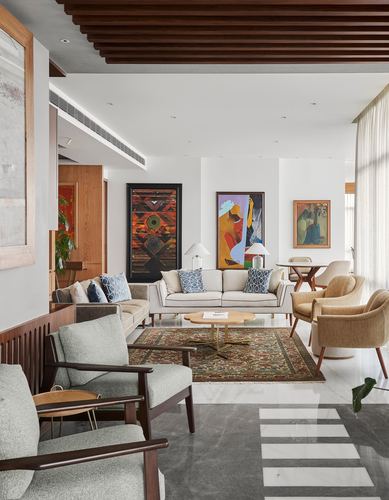Living room with slatted wood ceiling, gallery wall of art, beige sofas and mid-century armchairs on stone floor
