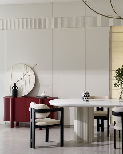 Dining area with fluted-base marble table, black chairs, round mirror over red sideboard