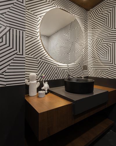 Powder room with black and white geometric tiled walls, backlit round mirror, and wood floating vanity with black basin
