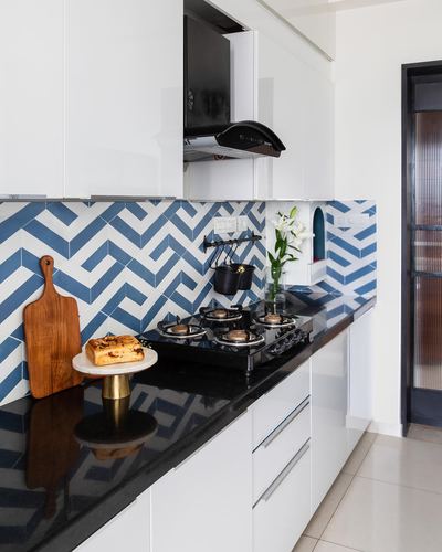 White modular kitchen with blue chevron tile backsplash, black countertop, gas stove, and styled cake stand