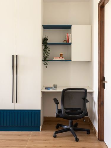 Compact built-in study nook with floating shelves, desk, black office chair, and teal fluted wardrobe panel