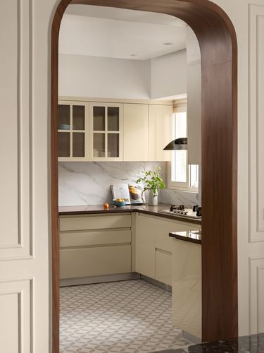View through a curved wood-clad archway into a cream kitchen with marble backsplash and patterned floor