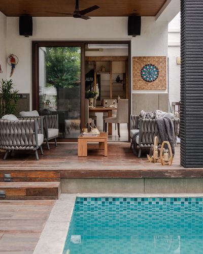 Covered poolside patio with woven armchairs, wood deck, and glimpse into dining area beyond glass doors