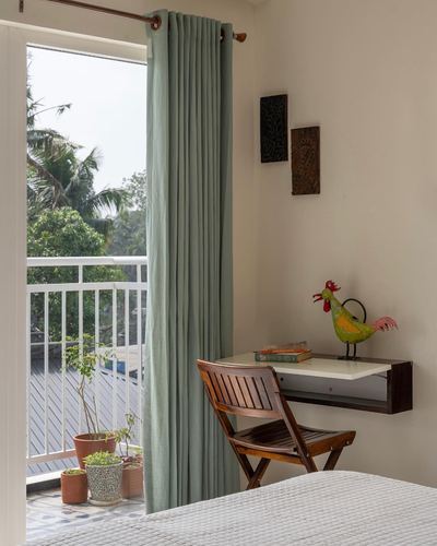 Bedroom corner with sage curtain, floating wood desk, folding chair and balcony view of trees