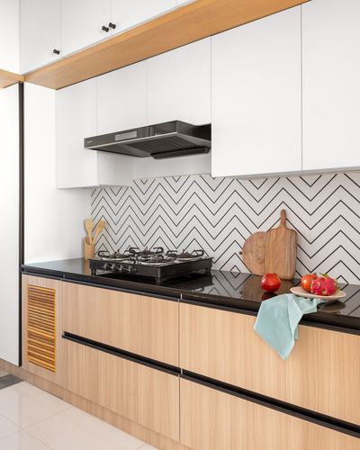 Modern kitchen counter with gas hob, chevron backsplash, black countertop and wood-toned cabinetry