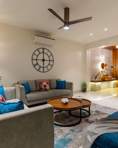 Living room with grey sofas, blue cushions, round wood coffee tables, and a lit statue niche beyond