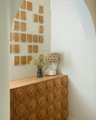 Arched foyer niche with textured wood wall tiles above a carved wood sideboard, vase and lamp on top