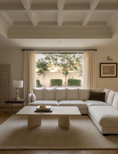 Cream living room with sectional sofa, travertine table, and coffered ceiling facing garden window