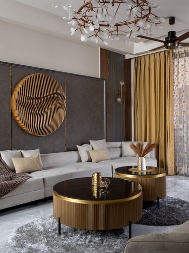 Living room with grey sectional, ribbed brass coffee tables, and circular wood sculpture on dark wall