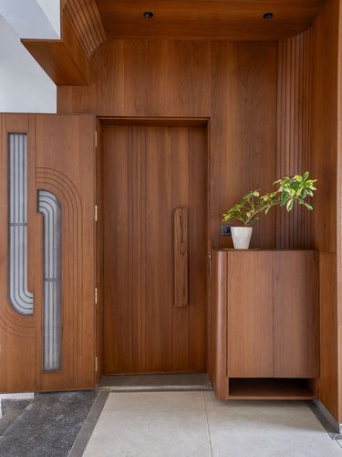 Wooden entrance foyer with carved main door, fluted panelling, floating cabinet and potted plant