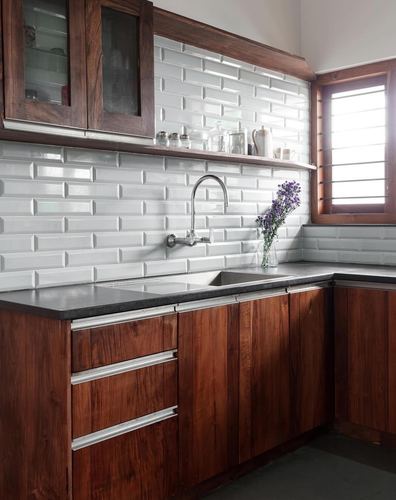 Wooden kitchen with white subway tile backsplash, black countertop, wall-mounted faucet, and flowers