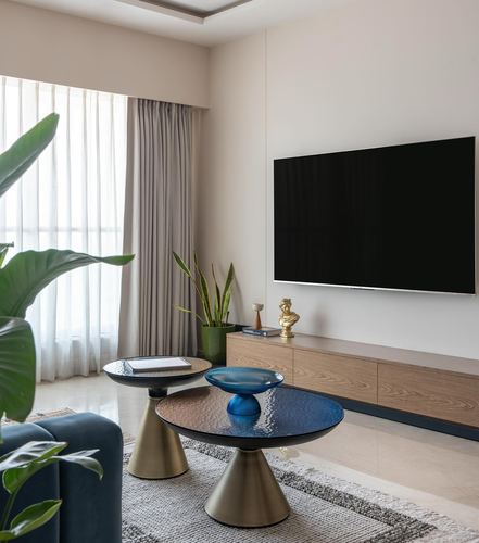 Living room with wall-mounted TV, wood console, and layered brass pedestal coffee tables on a rug