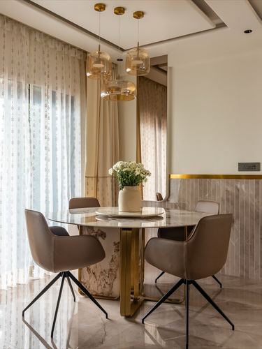 Round marble dining table with brass base under three amber pendant lights, taupe leather chairs around it