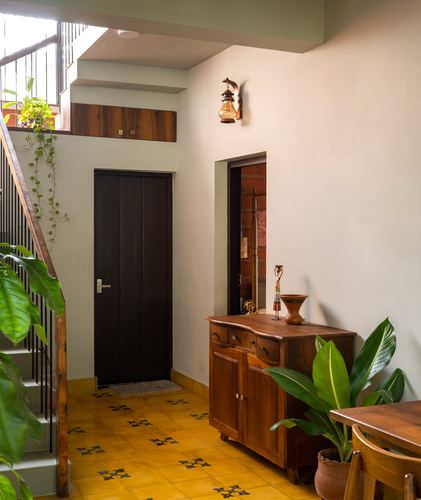 Foyer with patterned yellow tile floor, dark wood door, staircase and wooden sideboard with plants