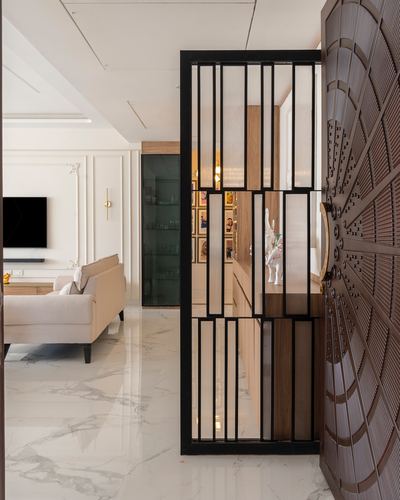 Black metal fluted screen and carved wooden door frame a marble foyer opening to a living room