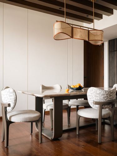 Dining table with stone top and oval cane-back chairs under a cane pendant light