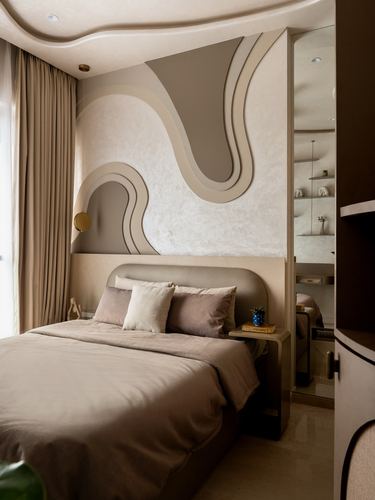 Curved beige plaster wall with organic wave motifs behind an upholstered bed in a soft-toned bedroom.