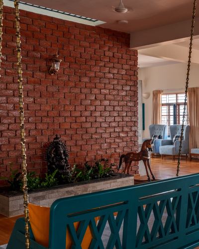 Foyer with exposed brick wall, brass lantern, teal jhula, and view into living room with cane chairs