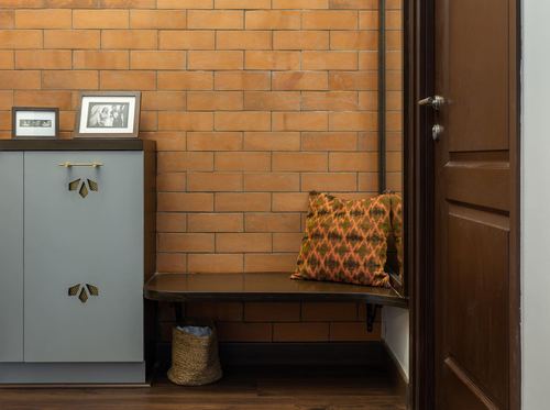 Foyer with terracotta brick wall, floating wooden bench, cane basket and blue-grey storage cabinet
