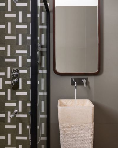 Bathroom with patterned green tile shower, wood-framed mirror, and carved stone pedestal sink