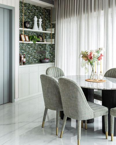 Dining table with green tweed chairs beside a mosaic-tiled open shelving unit and sheer curtains