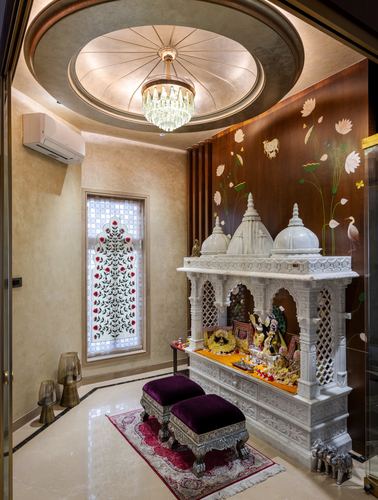 Ornate white marble temple mandir beneath a round crystal chandelier ceiling in a pooja room