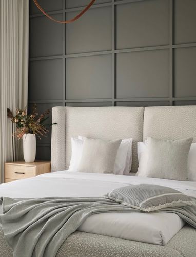 Bed with wide boucle headboard against grey paneled wall, white bedding and sage throw