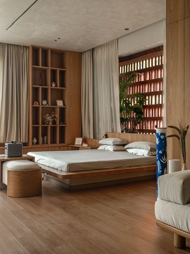 Wood-panelled bedroom with platform bed, open shelving, and sheer curtains before a perforated brick screen