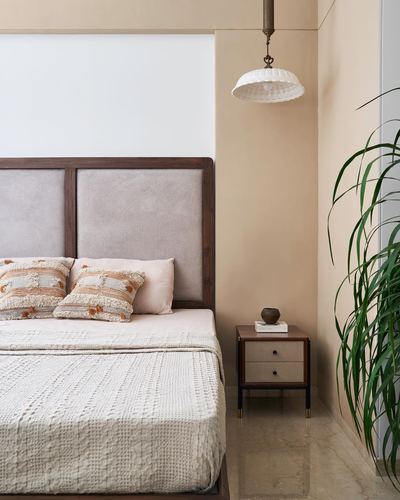 Beige-toned bedroom with wood-framed upholstered headboard, pendant lamp, and bedside plant