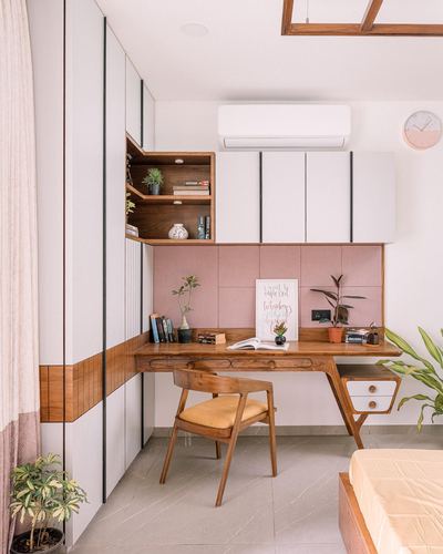 Wooden study desk under pink upholstered panel with white cabinetry and wall clock