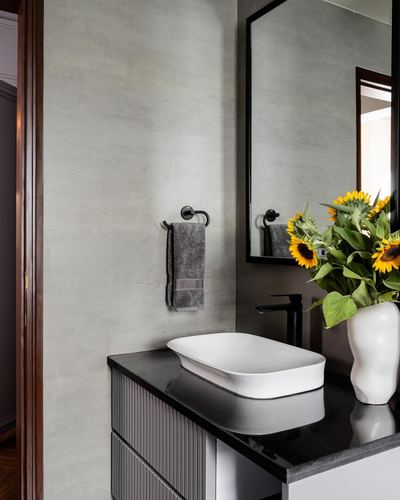 Bathroom vanity with black countertop, white vessel sink, black mirror, and sunflowers