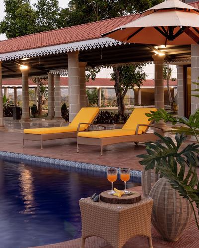 Poolside terrace with yellow chaise loungers, umbrella, and colonnaded terracotta-roofed veranda at dusk